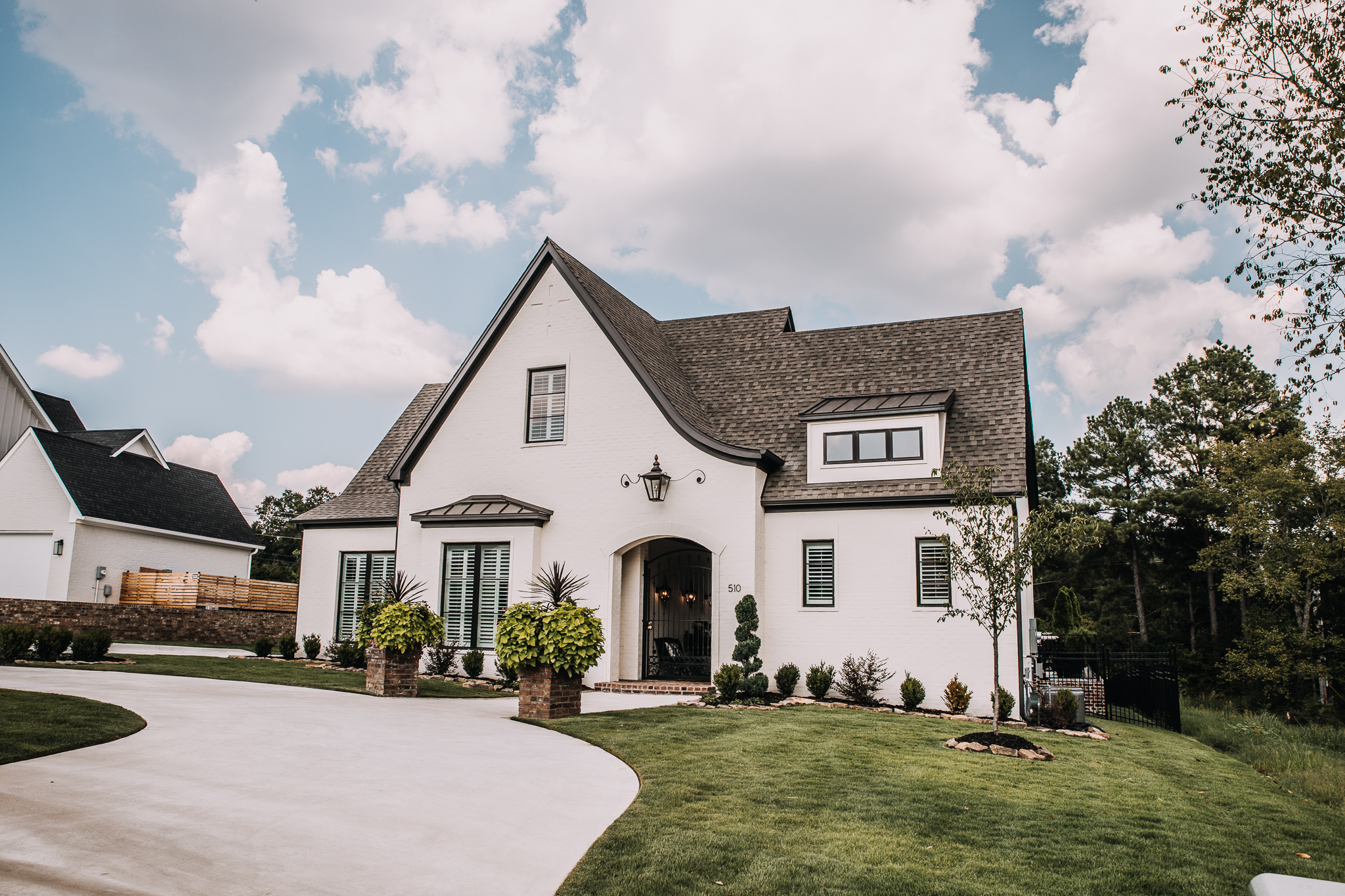 White brick custom home with steep gables, arched entry and manicured lawn